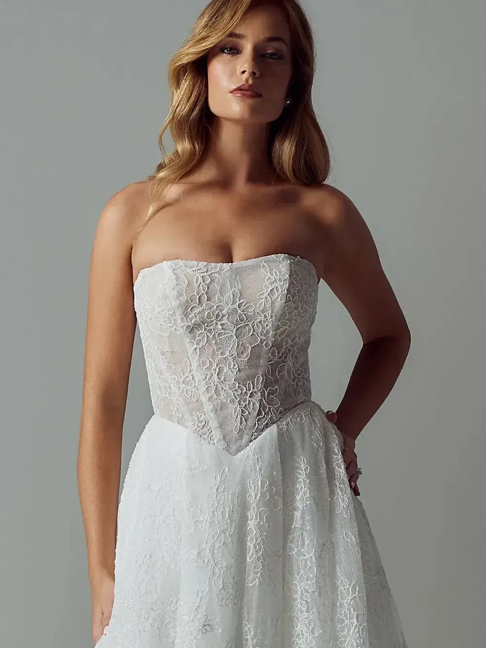 A woman wearing a strapless white dress with floral lace detailing.