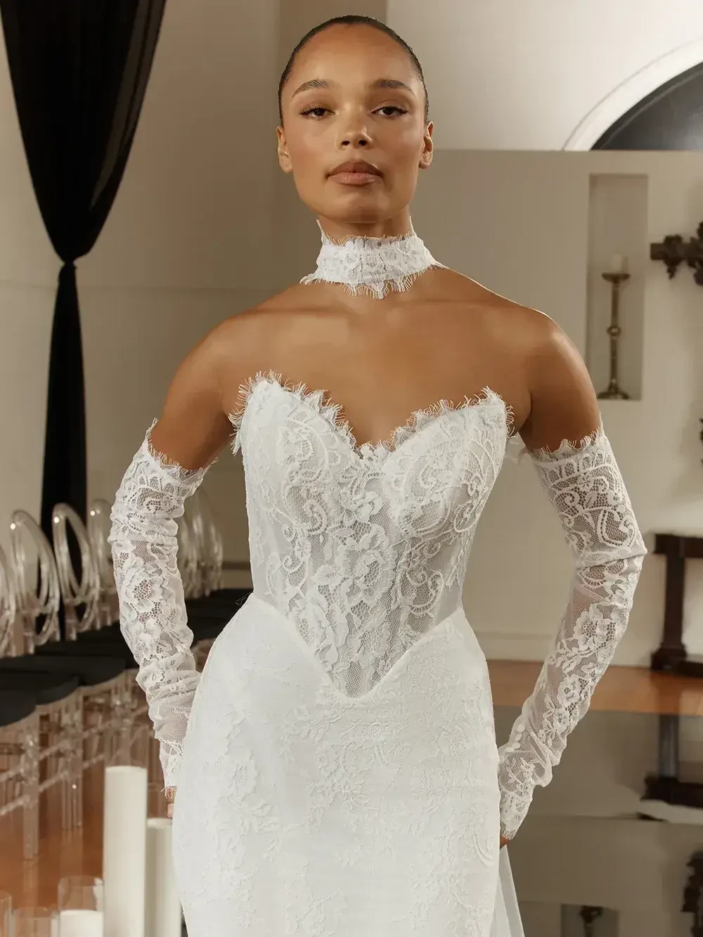 A model wearing a white lace wedding gown with a sweetheart neckline and long lace gloves.