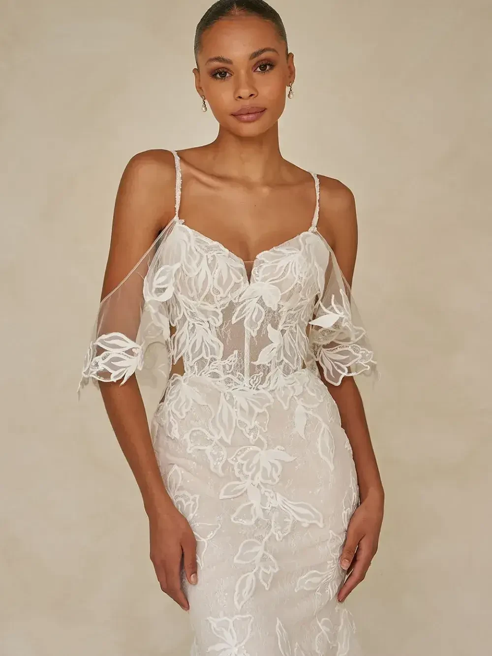 A woman wearing an elegant wedding dress with sheer sleeves and floral patterns.